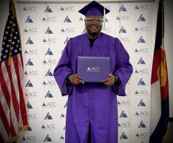 Ayanda Dladla-Ndlovu, ACC Alum, wearing purple regalia in front of ACC banner