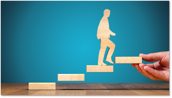 Wooden person walking up wooden steps with hand holding the top step