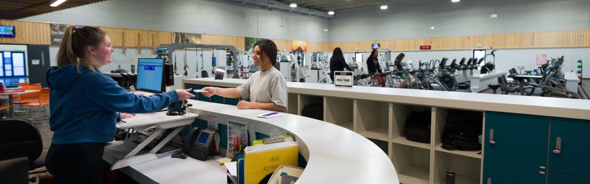 ACC Fitness Center employee interacting with ACC student at the front desk of the Fitness Center at the Littleton Campus.