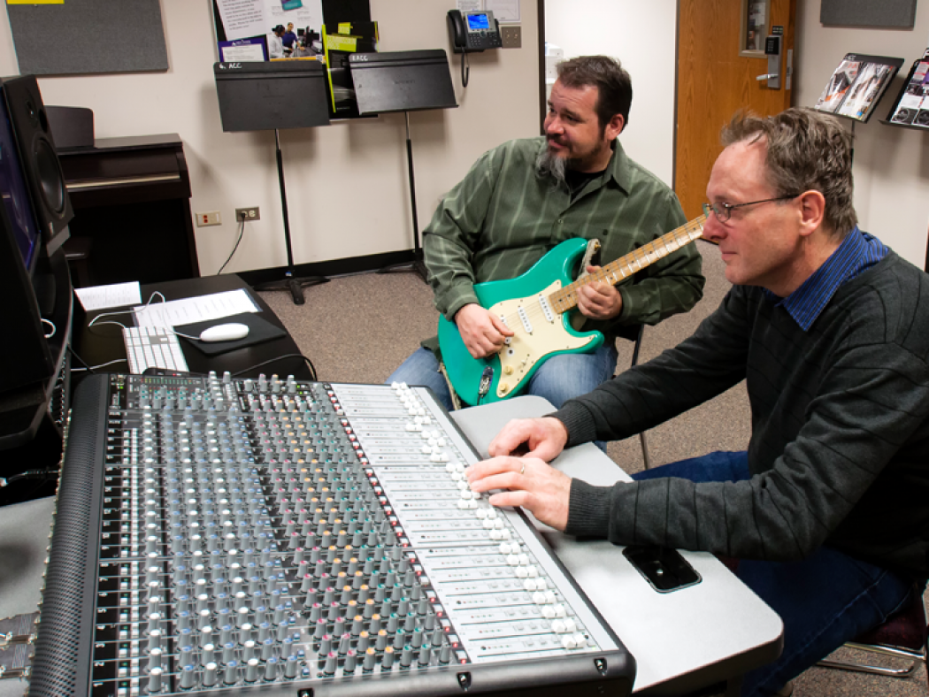 ACC faculty and students in the Music Audio Technology lab playing guitar and working a sound board.