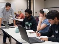 ACC students in class with laptops on desks and a faculty member talking to them.