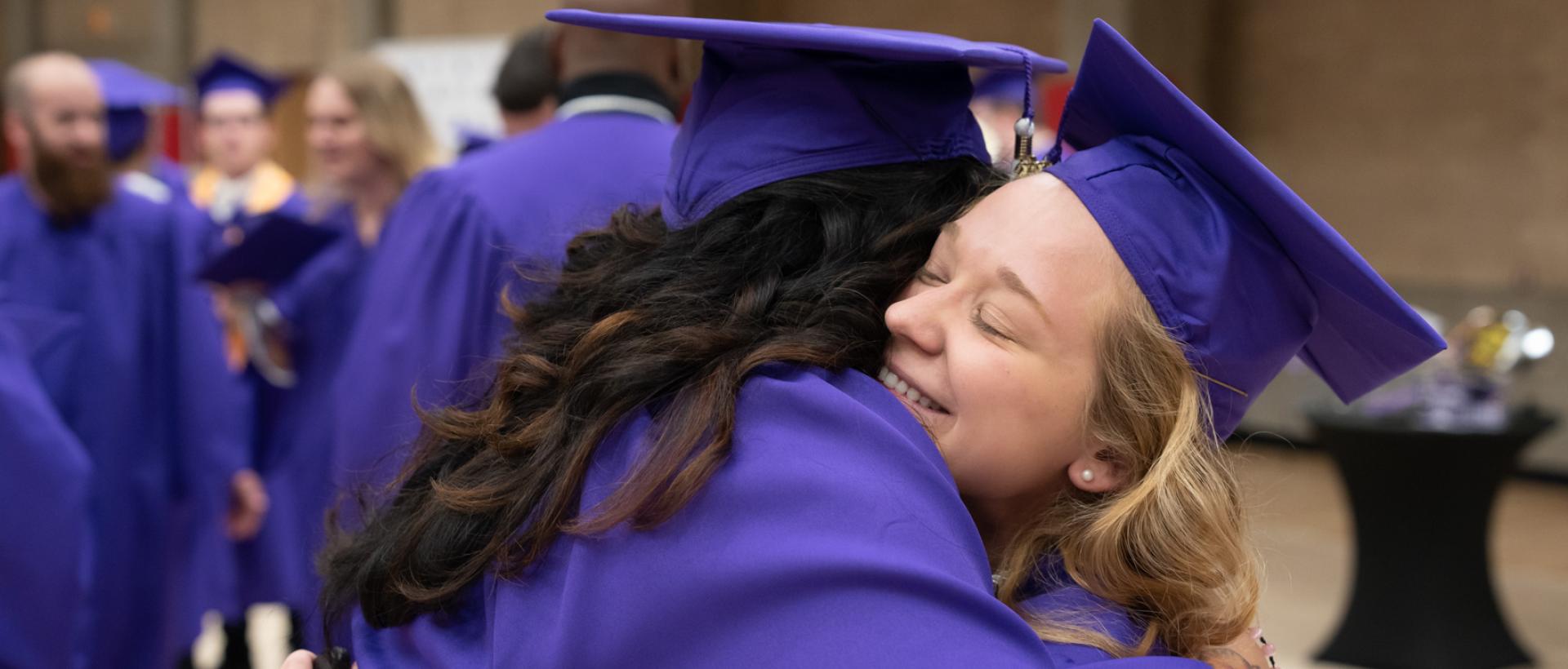 Two ACC graduates hugging at ACC's Commencement ceremony.