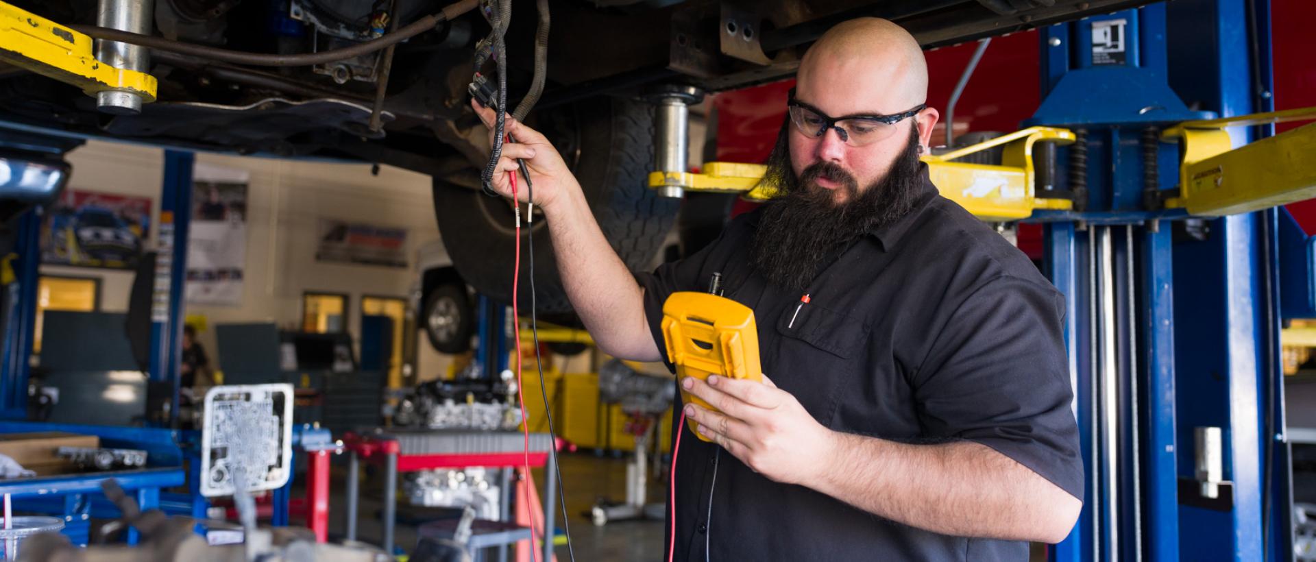 ACC student using tools to check a car on a lift in the Littleton Campus Auto Technology garage