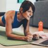 Woman doing a plank while using ACC Sweat On Demand workout videos on laptop.