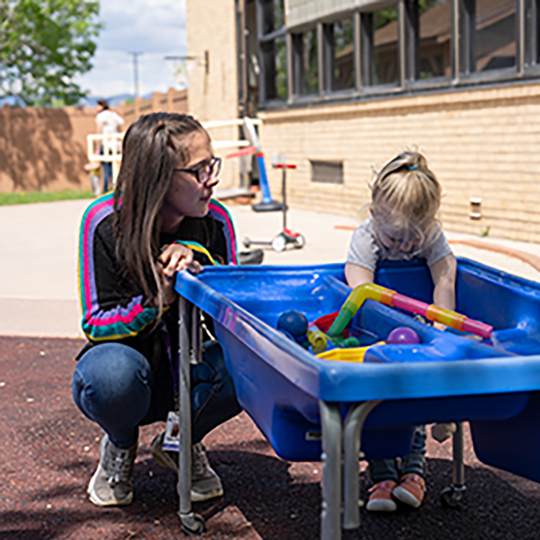 ACC early childhood educator working with child at sensory table at the Child Development Center at the Littleton Campus.